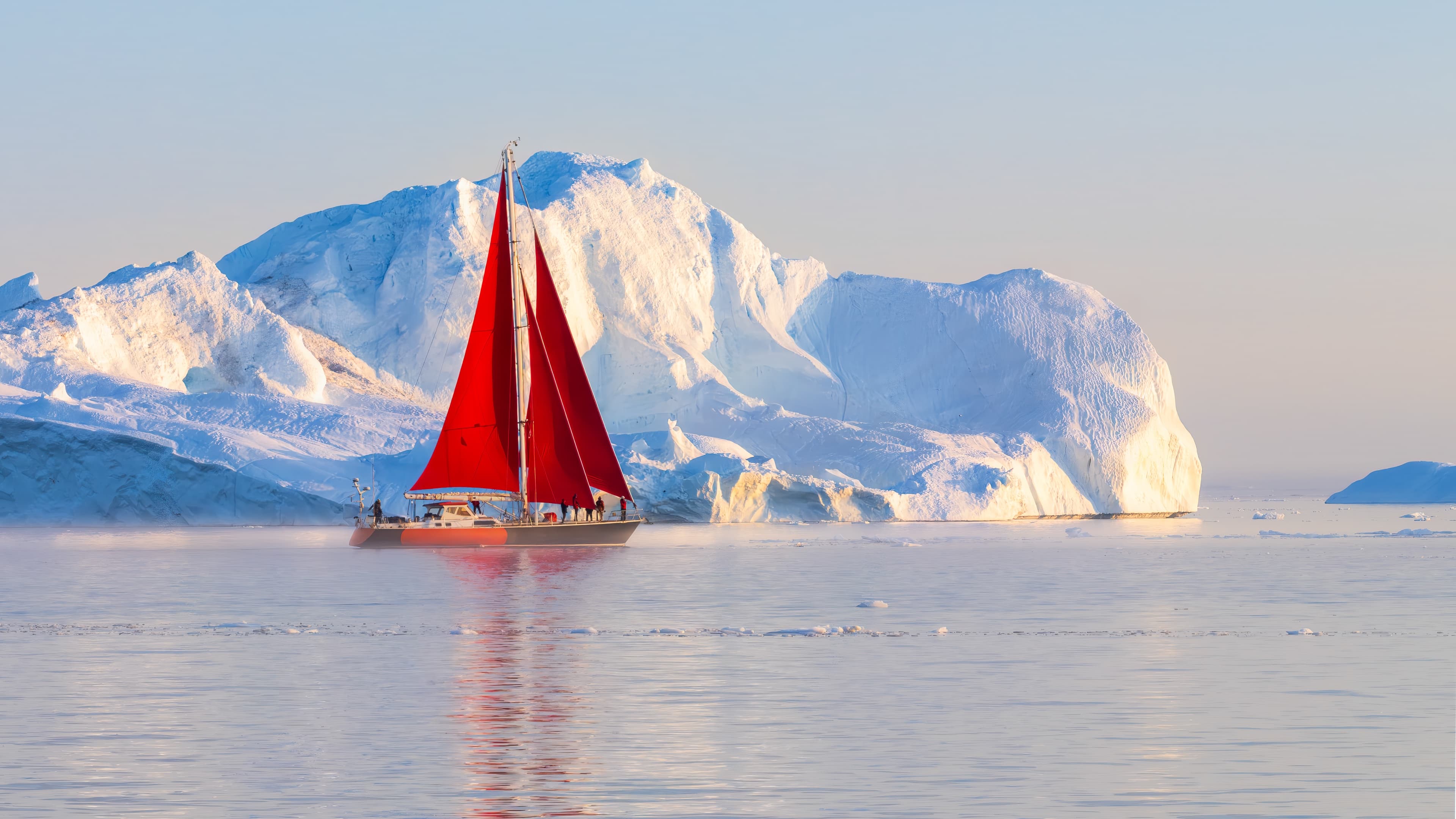 Red sailboat at golden sunset among Greenland icebergs